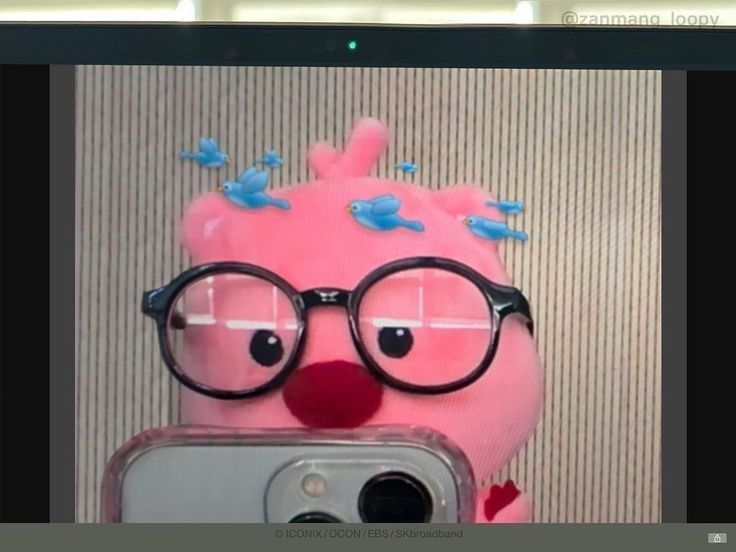 a pink stuffed animal with glasses taking a selfie in front of a cell phone