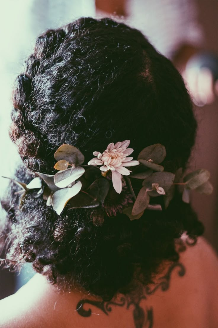 the back of a woman's head with flowers and leaves in her hair,