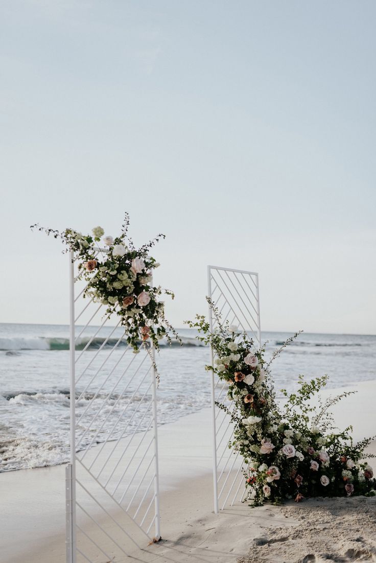 an outdoor ceremony setup on the beach with flowers and greenery in front of it