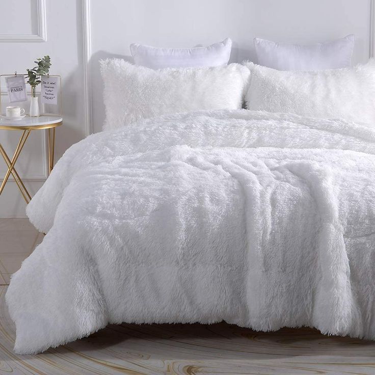 a white bed with fluffy pillows and blankets on top of it in a room next to a table