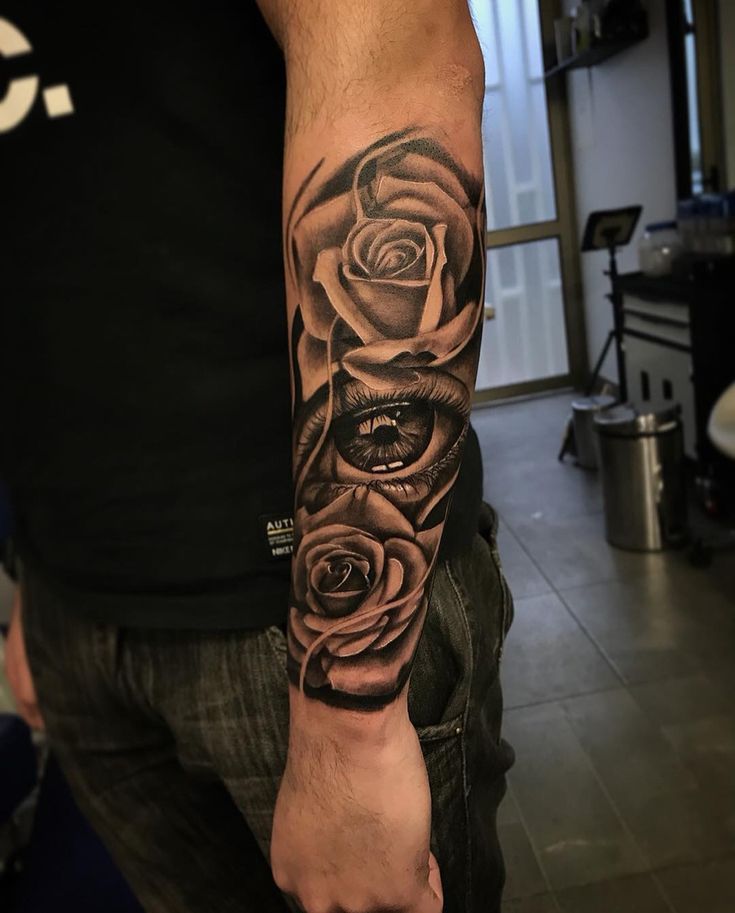 a man with a black and grey rose tattoo on his arm, in a room