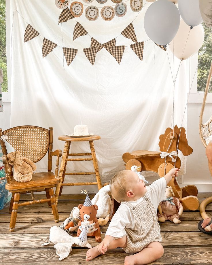 a baby sitting on the floor with balloons and stuffed animals