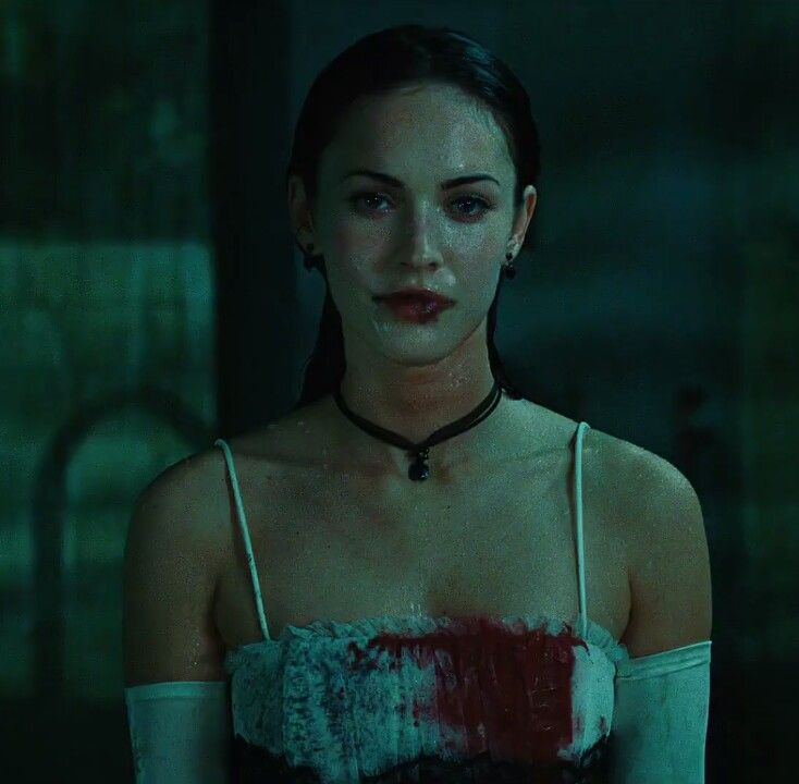 a woman with blood on her chest wearing a choker in a dimly lit room