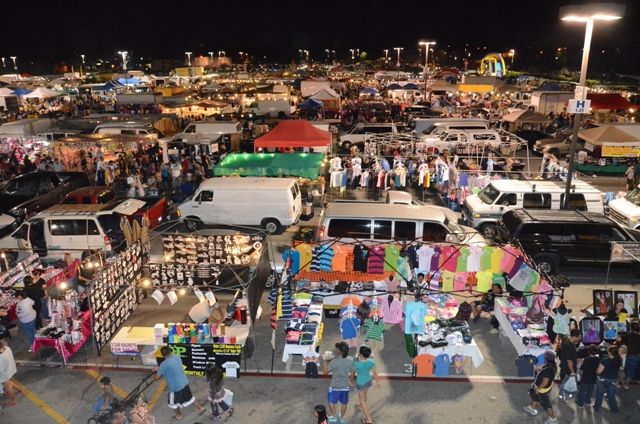 a large group of people standing around in a parking lot with many tents and cars