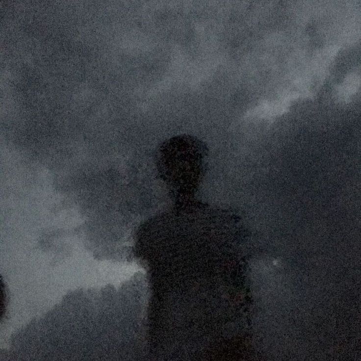 the silhouette of a person standing in front of a dark sky with clouds behind them