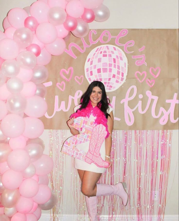 a woman standing in front of a pink and white backdrop with balloons on the wall