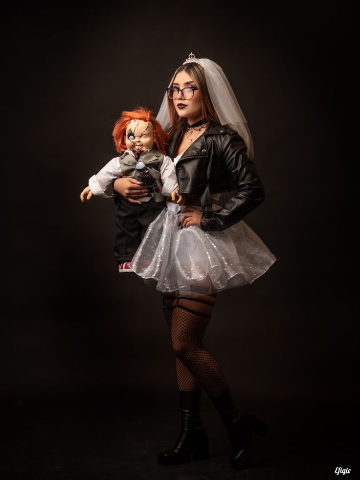 a woman in a wedding dress holding a doll and posing for a photo on a black background