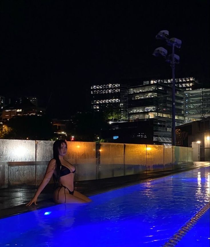 a woman sitting on the edge of a swimming pool at night