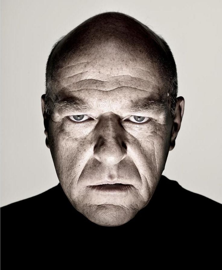 an older man with blue eyes stares at the camera while standing in front of a white background