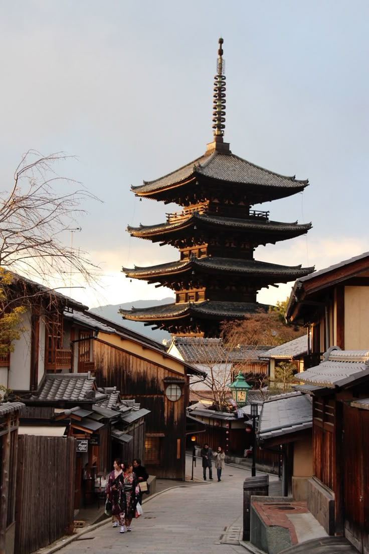 a tall pagoda towering over a city next to other buildings and people walking down the street