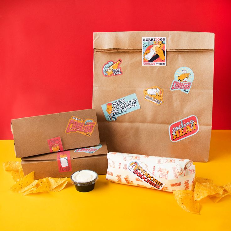 a brown paper bag with stickers on it next to some chips and a cup