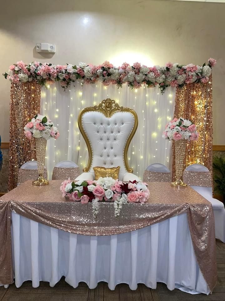 a table topped with a white chair covered in pink flowers and gold sequins