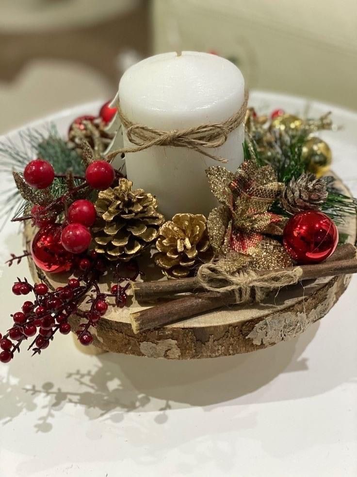 a white candle sitting on top of a wooden bowl filled with pine cones and berries