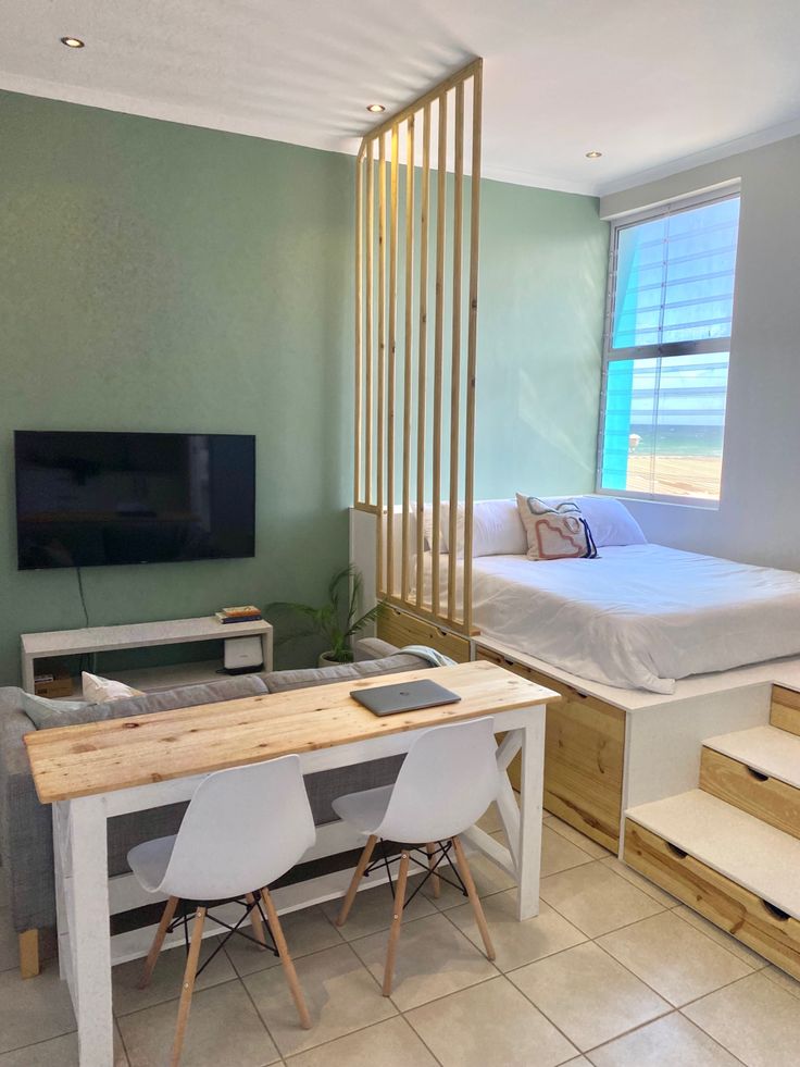 a room with two beds, a desk and stairs in front of a tv on the wall