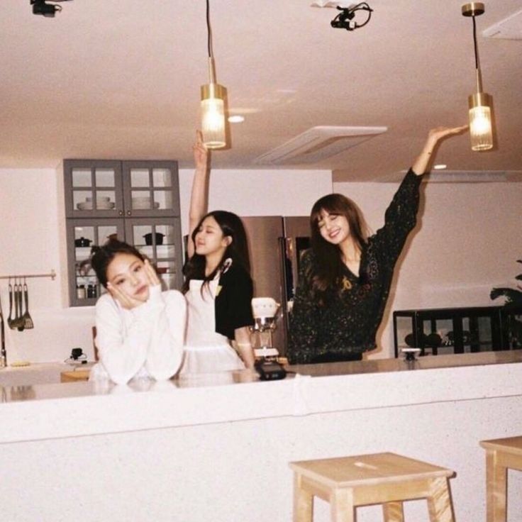 three women standing in a kitchen with one pointing up at the camera and another smiling