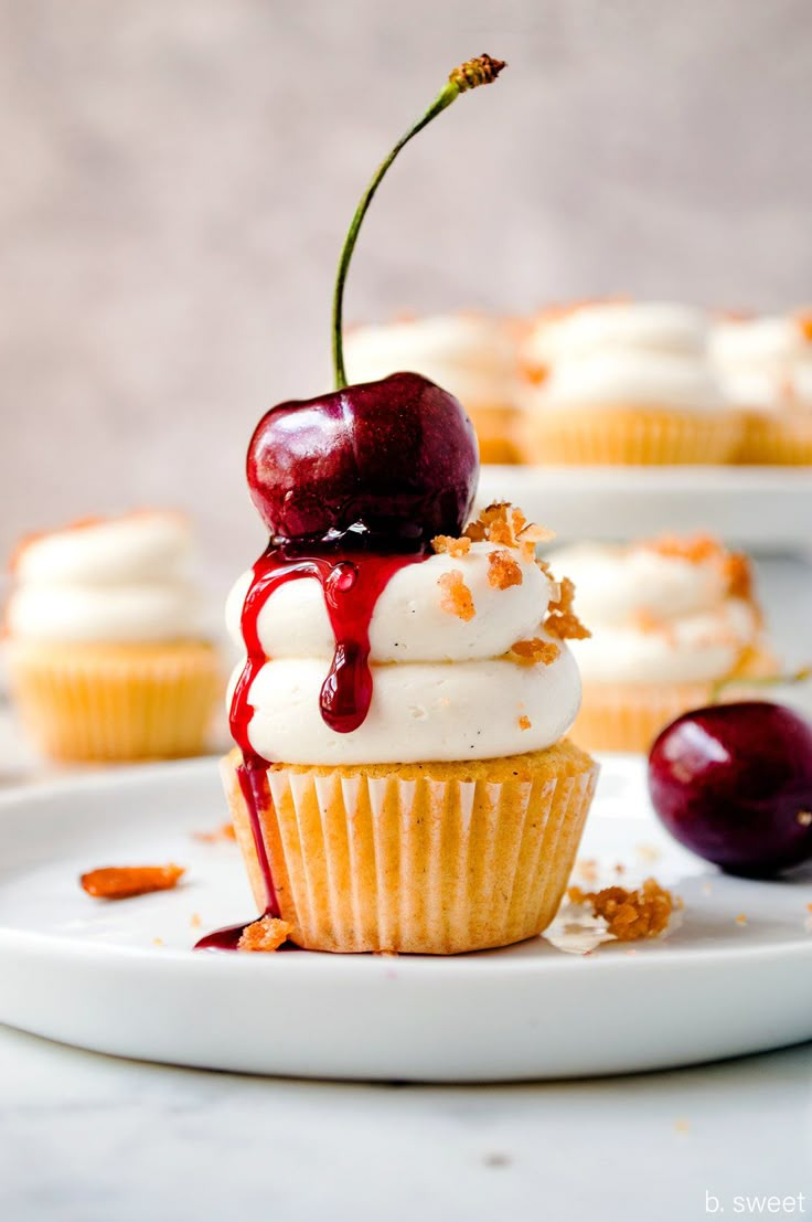 a cupcake with white frosting and cherries on top sitting on a plate