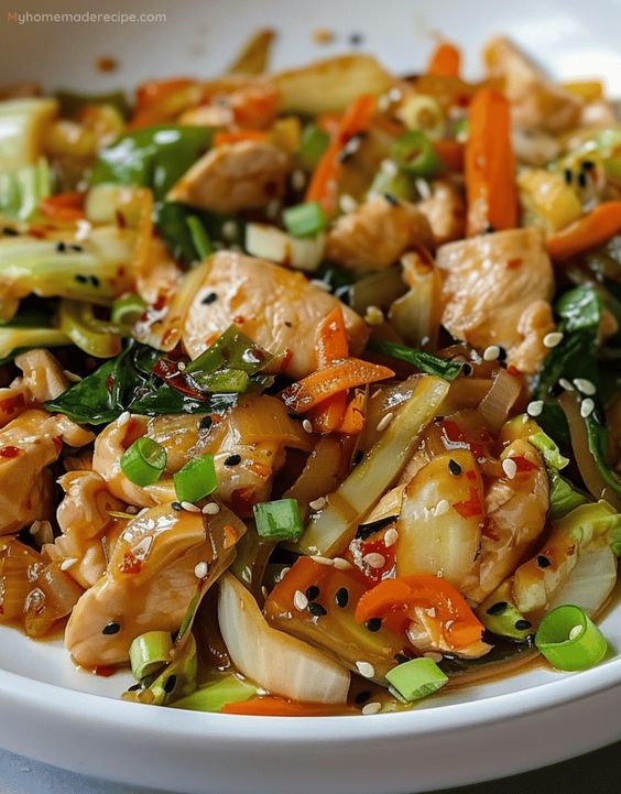 a white plate topped with chicken and veggies covered in sesame seed seeds on top of a table