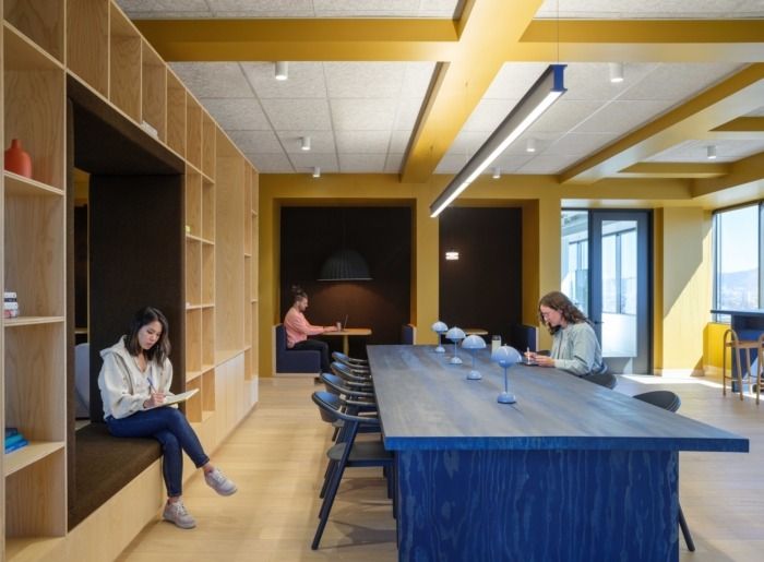 two women are sitting at a long table in the middle of a room with bookshelves