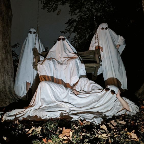 three ghostly people sitting on the ground in front of a tree and some leaves at night