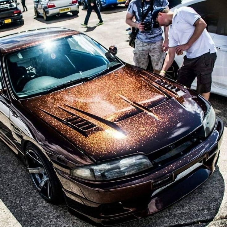 two men are standing next to a car with gold paint on it's hood