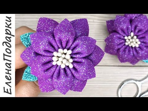 two purple flowers with white center being held by someone's hand next to scissors