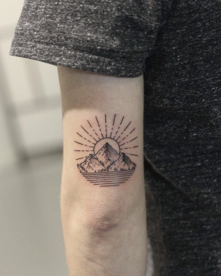 a person with a small tattoo on their arm that has mountains and sun in the background