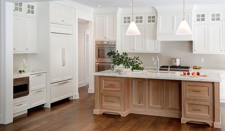 a large kitchen with white cabinets and wood flooring, along with an island in the middle