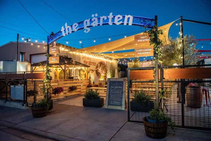 the entrance to an outdoor restaurant with lights strung over it and potted plants on either side