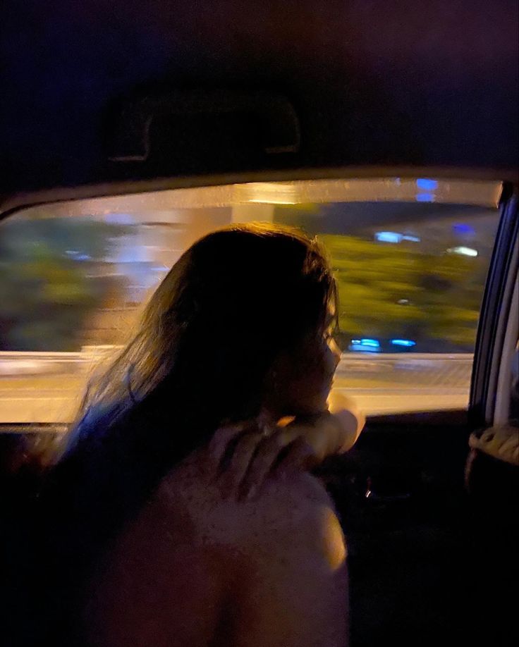 a woman sitting in the back seat of a car talking on her cell phone at night