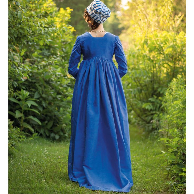 a woman in a blue dress and bonnet is walking through the grass with her back to the camera