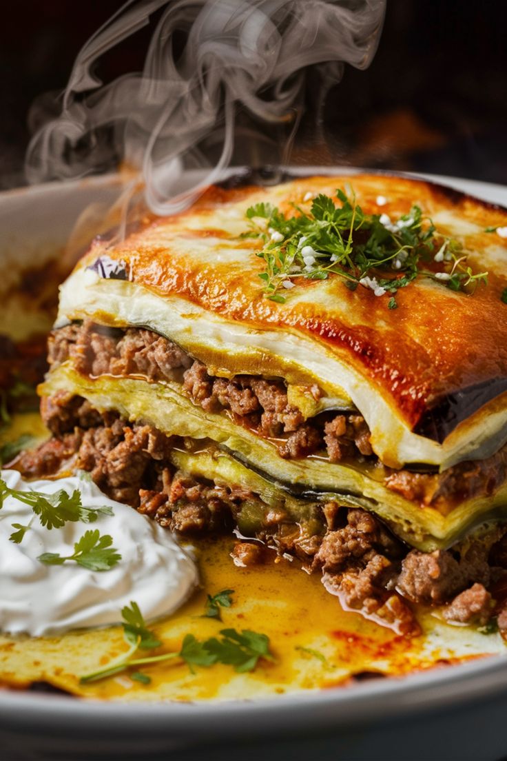 Steaming slice of lasagna with a dollop of sour cream, garnished with fresh herbs. Veggie Moussaka Recipe, Moussaka Recipe Greek Easy, Greece Food Traditional, Musaka Recipe, Moussaka Recipe Greek, Traditional Greek Moussaka Recipe, Greek Moussaka Recipe, Veggie Moussaka, Moussaka Recept