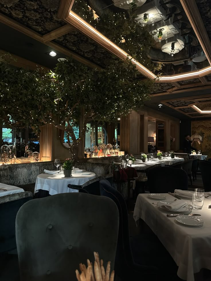 an empty restaurant with tables and chairs covered in white tablecloths, surrounded by trees