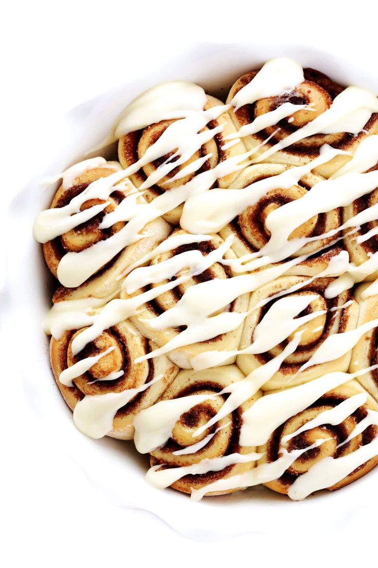 a white bowl filled with cinnamon rolls covered in icing