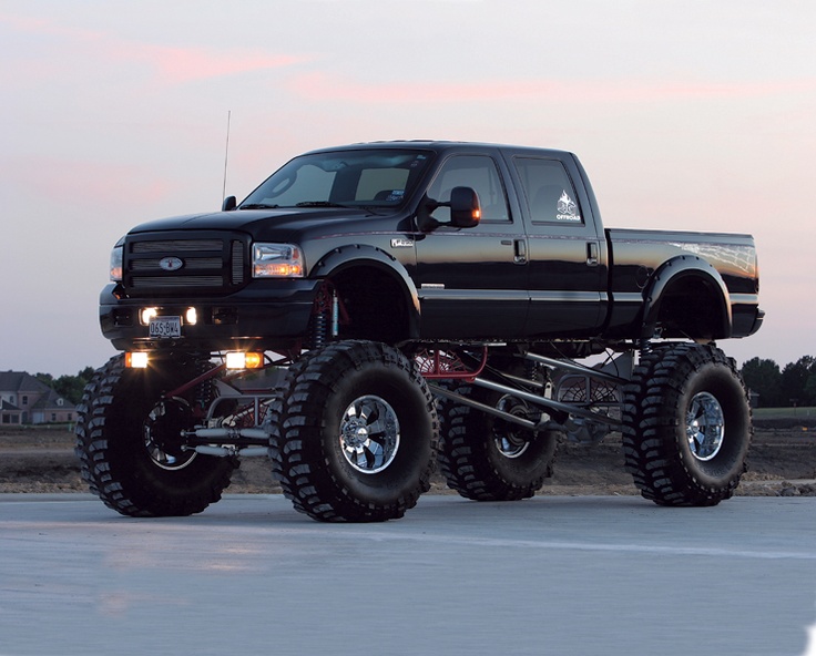 a large black truck with big tires on the road