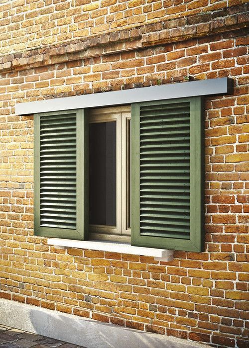 an open window on the side of a brick building with green shutters and white trim