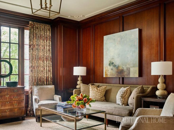 a living room with wood paneling and couches, coffee table, lamps, and paintings on the wall