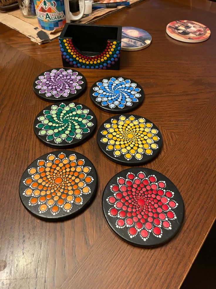 four coasters with beaded designs on them sitting on a table next to a cup