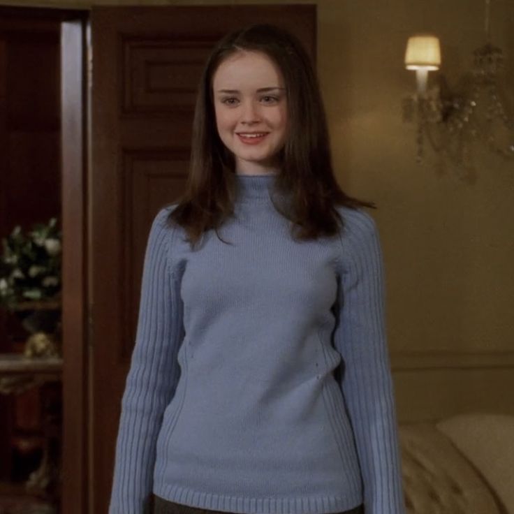 a woman standing in a living room wearing a blue sweater