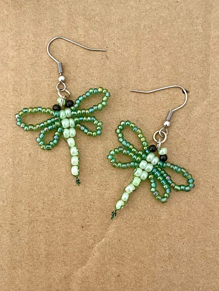 two green dragon shaped earrings with beads and bead work on the ends, sitting on a brown surface