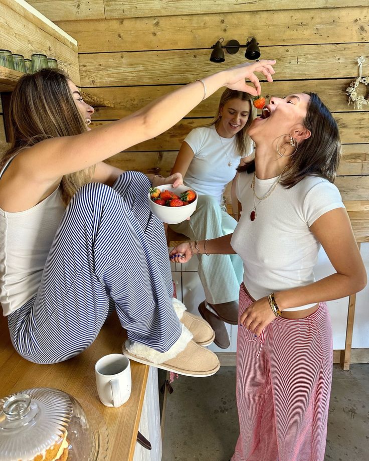 three girls are eating fruit in the kitchen together and one girl is reaching for something