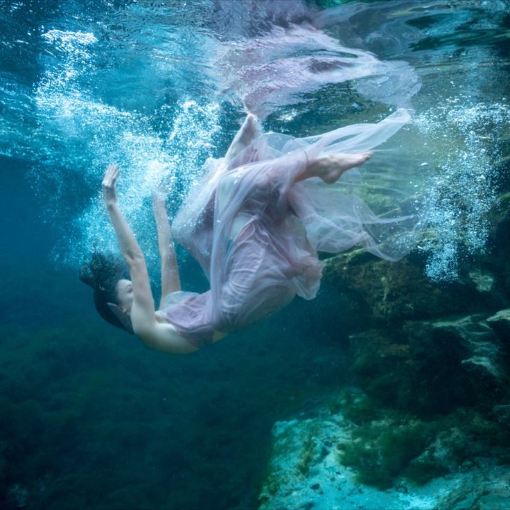 a woman in a pink dress swims under water