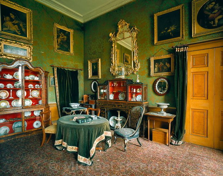 a room with green walls and pictures on the wall, including an old fashioned dining table