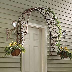 an iron arch with flowers hanging from it's sides on the side of a house