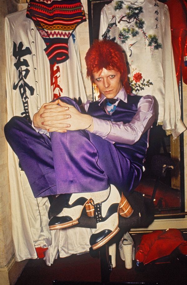 a man with red hair sitting on top of a mannequin wearing purple pants