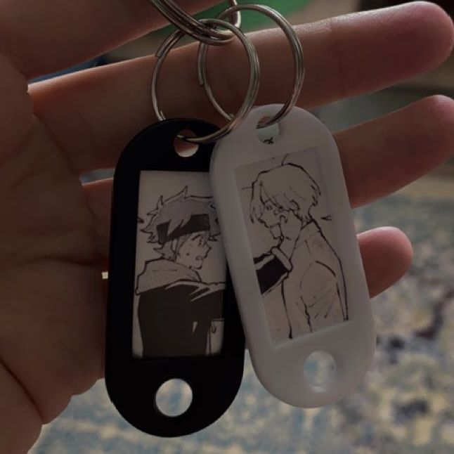 a hand holding a black and white keychain with an anime picture on it