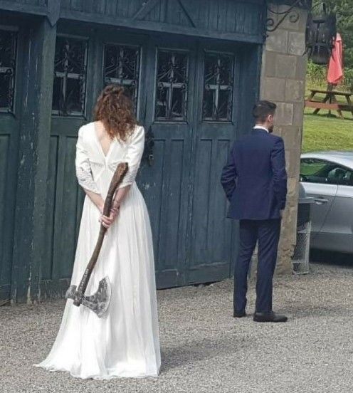 a woman in a long white dress holding an old fashioned hammer standing next to a man in a suit