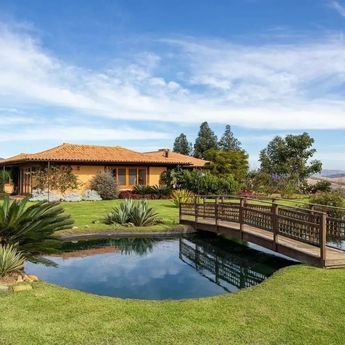 a wooden bridge over a small pond in front of a house with a gazebo