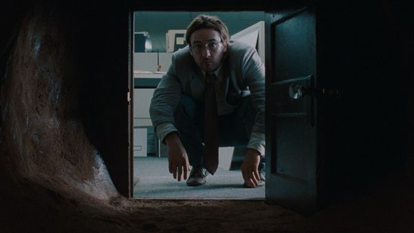 a man in a dark room with his hands on the ground looking into a door