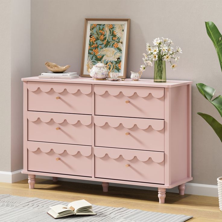 a pink dresser with flowers on top and a plant in the corner next to it