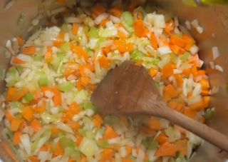 a wooden spoon in a pot filled with chopped carrots and celery,